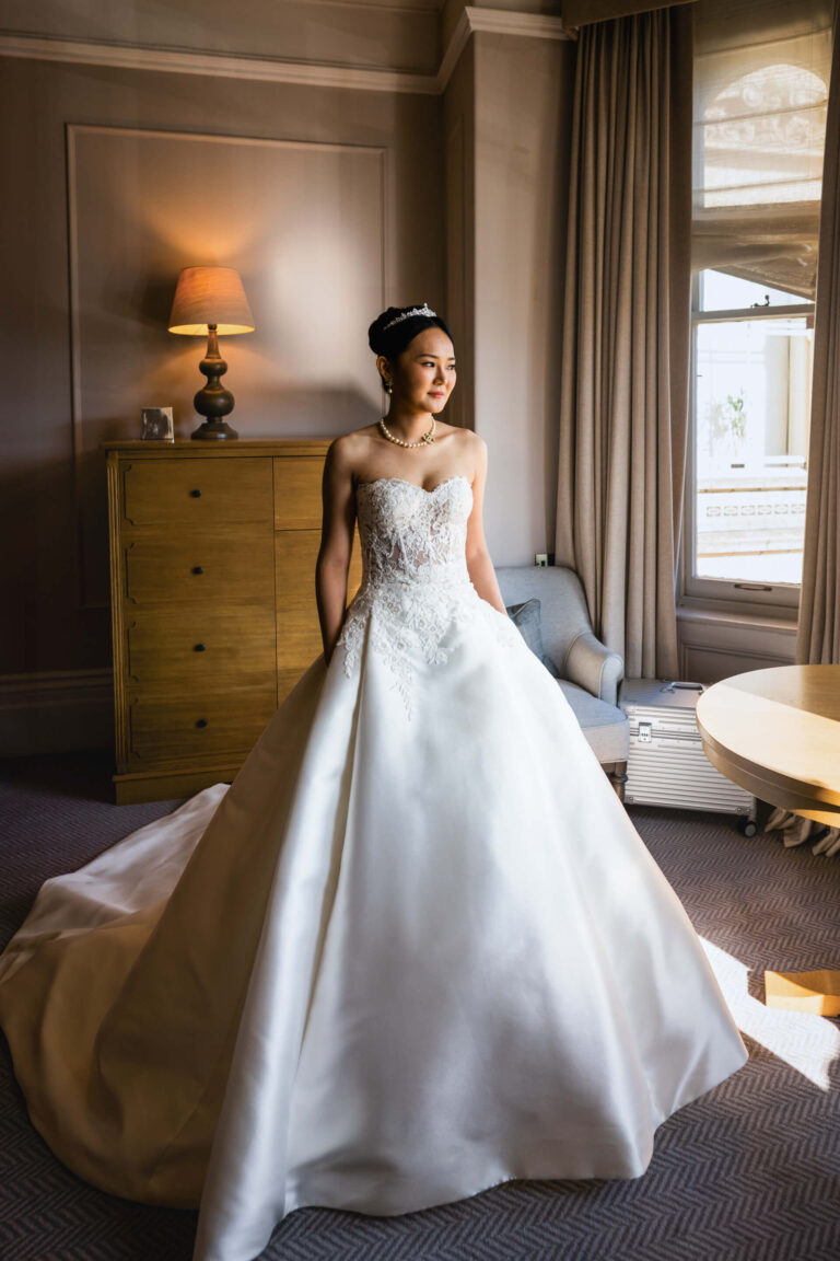 Bride in elegant white wedding dress, standing indoors.