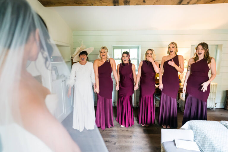 Bridesmaids react excitedly to bride's dress reveal.