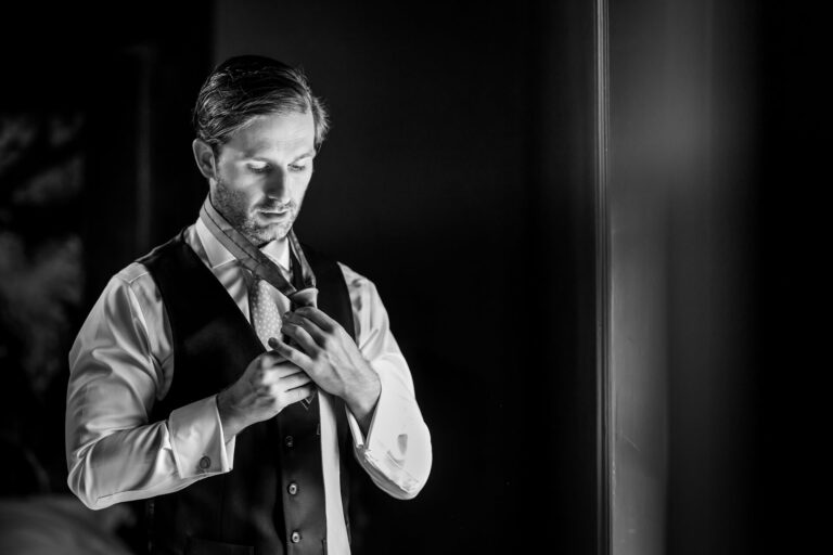 Man adjusting tie in black and white photo.