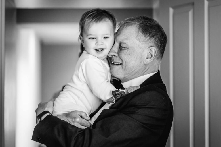 Grandfather hugging smiling infant indoors.