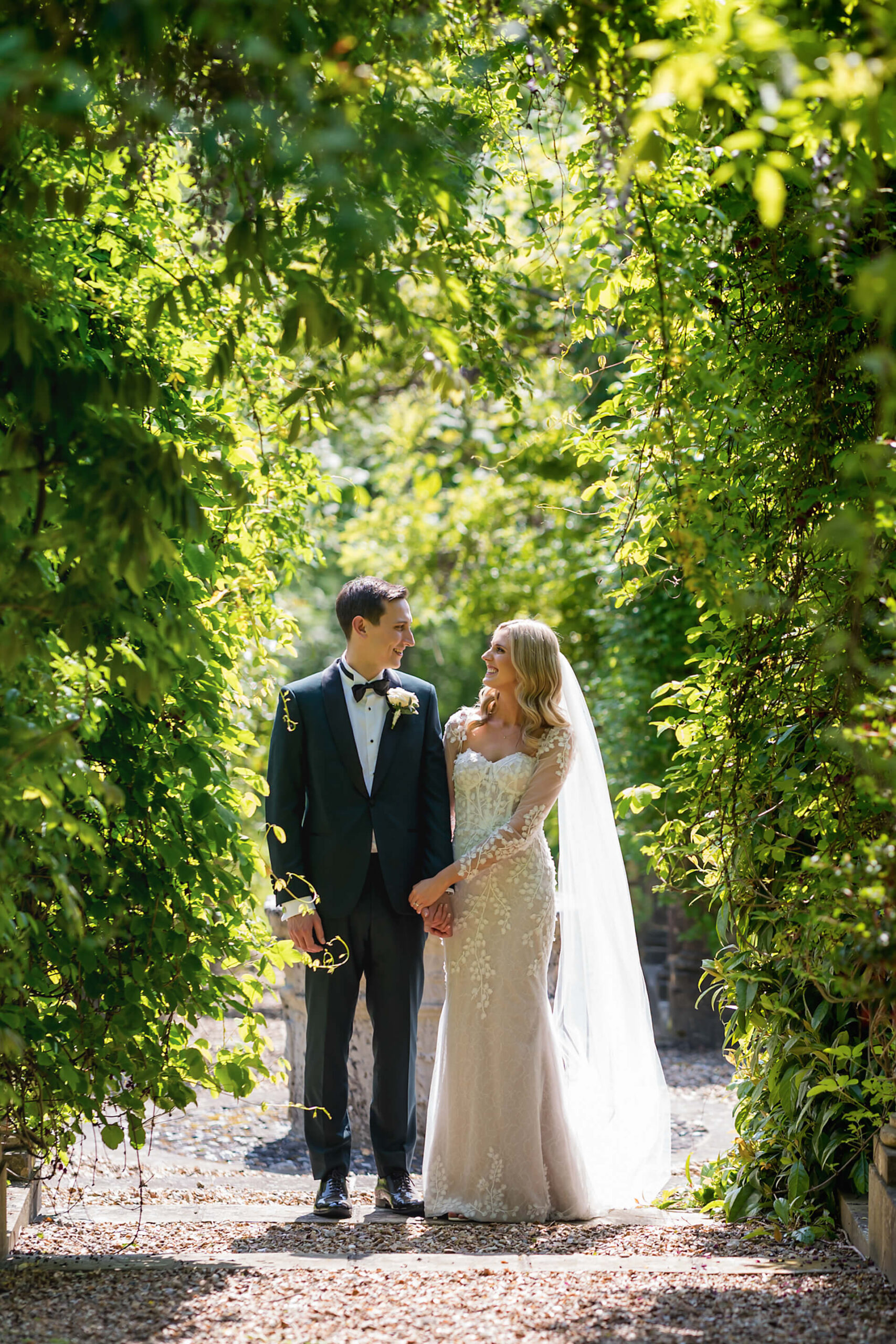 Couple in wedding attire under leafy arch.