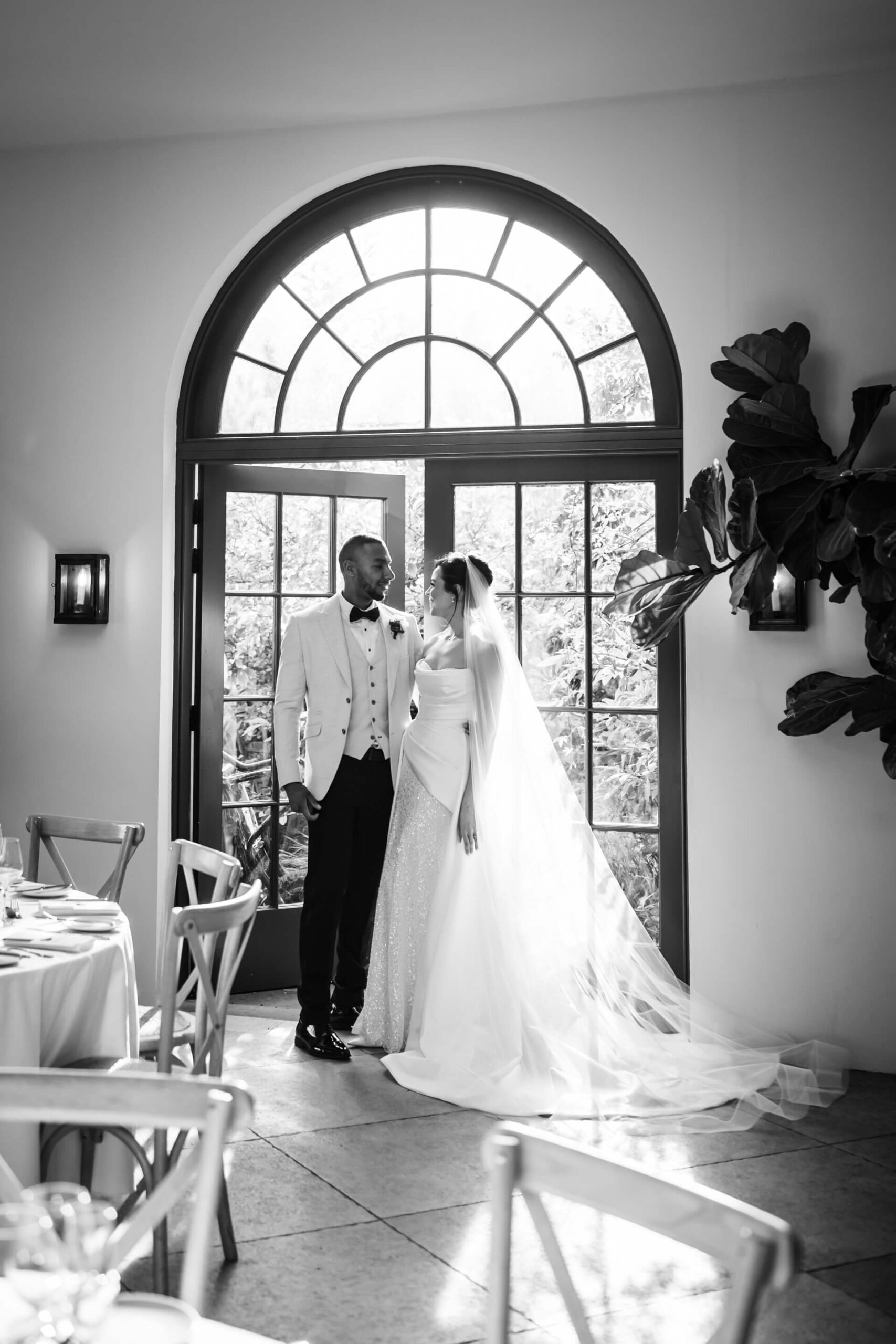 Bride and groom in front of arched window.