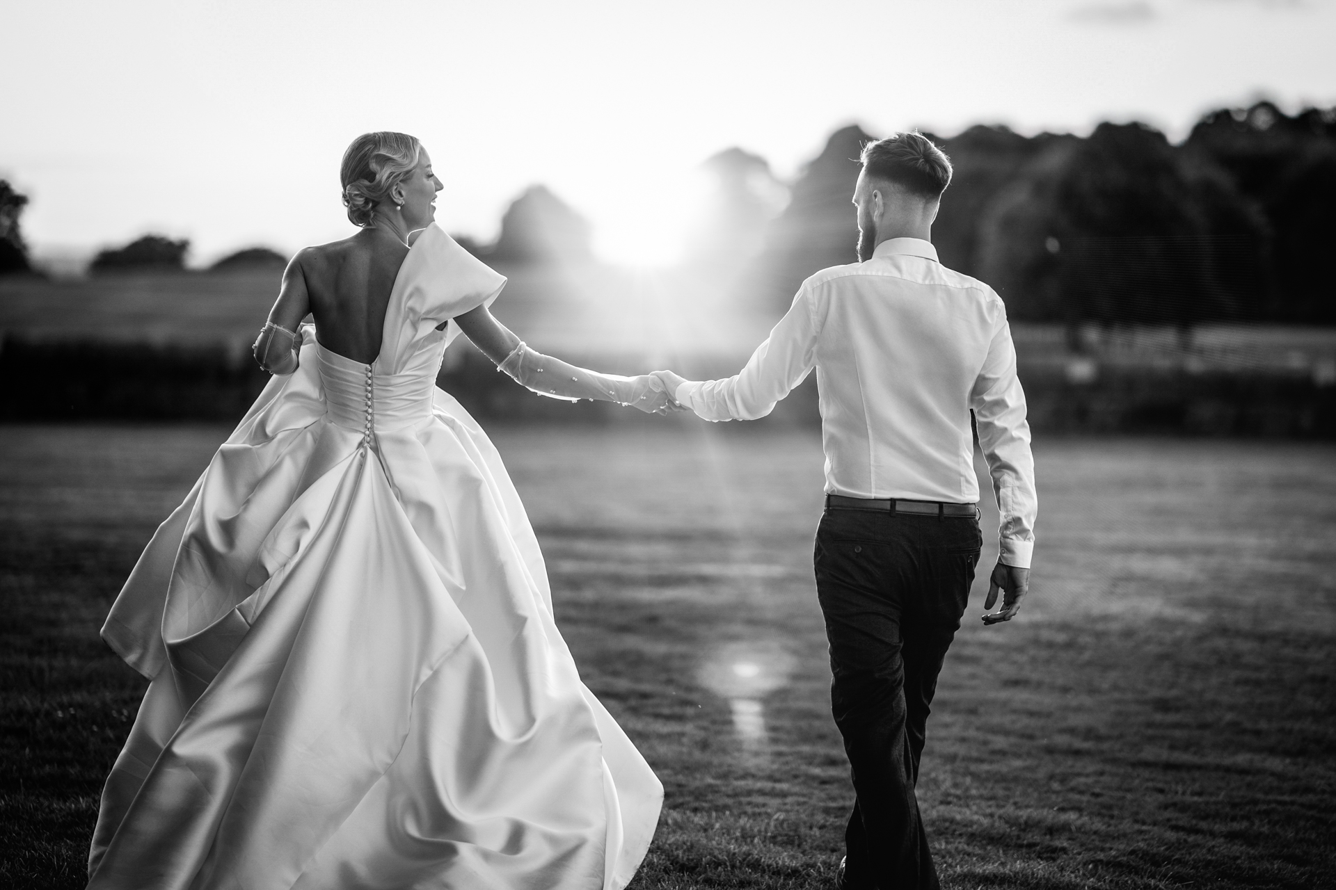 Bride and groom walking at sunset, holding hands.