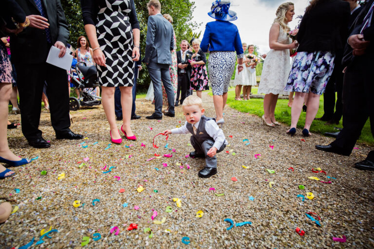Child playing with colourful confetti at outdoor event.