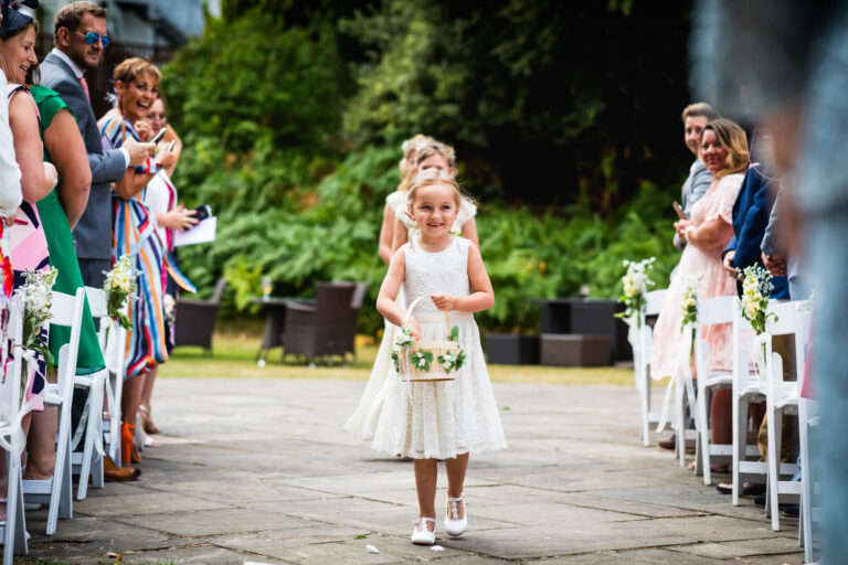 Young flower girl walking down wedding aisle