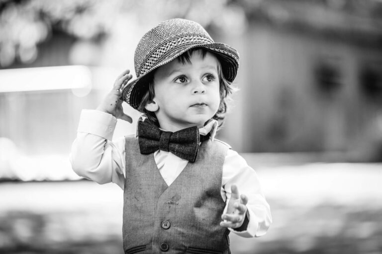 Young child in hat and bow tie outdoors.