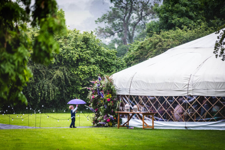 Child with umbrella near yurt on rainy day
