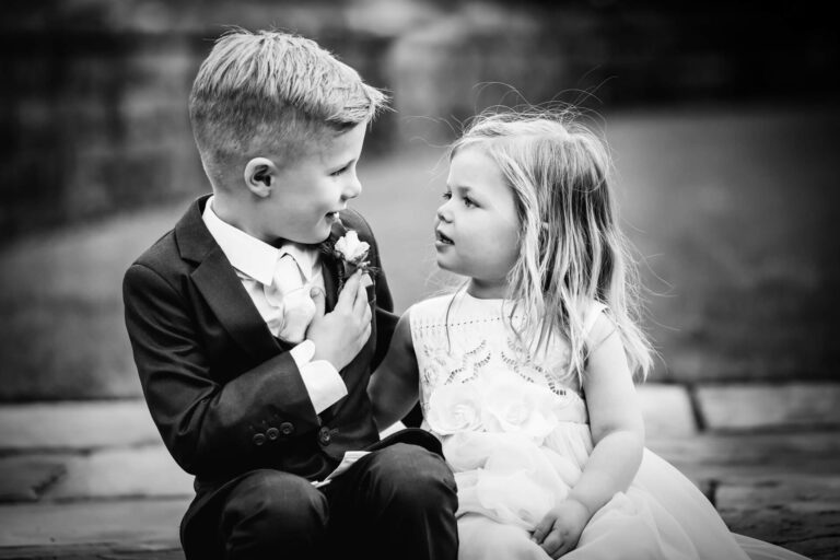 Two children dressed formally, smiling at each other.