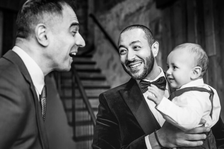 Men smiling and holding a baby at event.