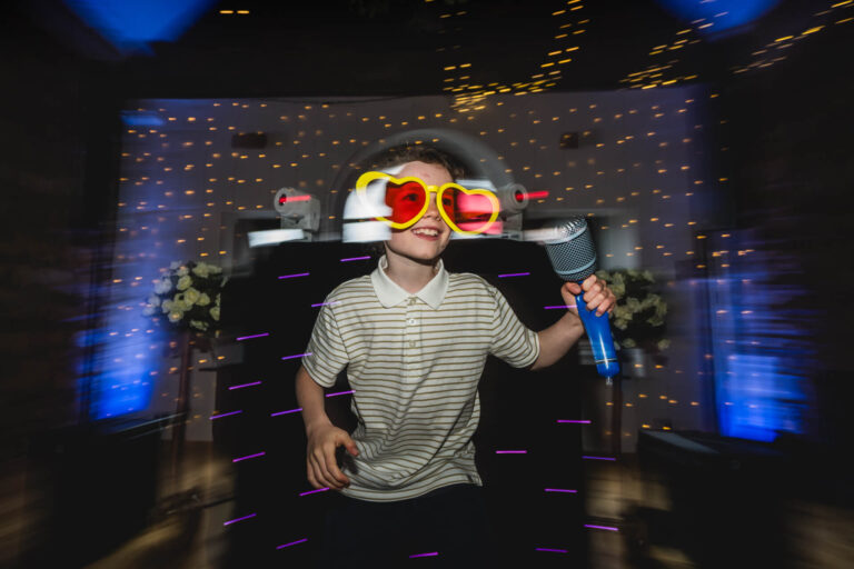 Child wears heart glasses, holding a toy microphone.