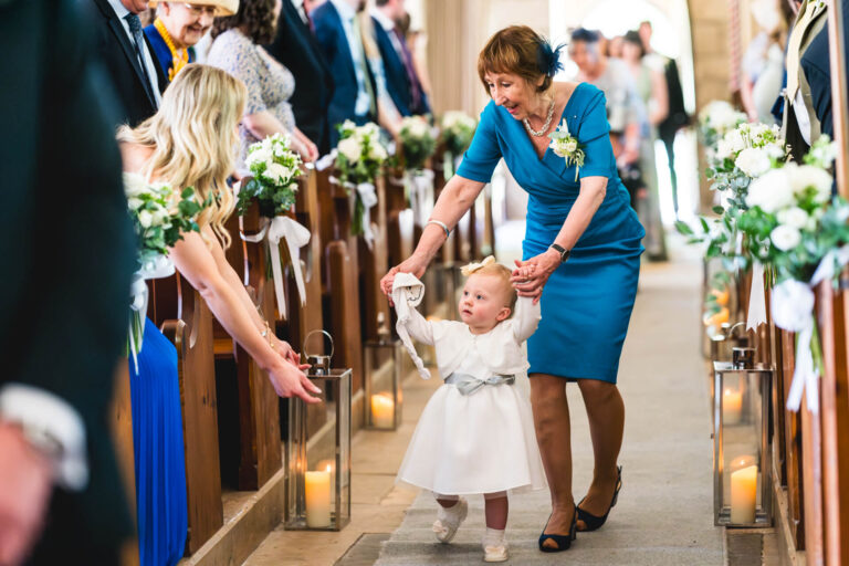 Woman helping child walk down decorated aisle.