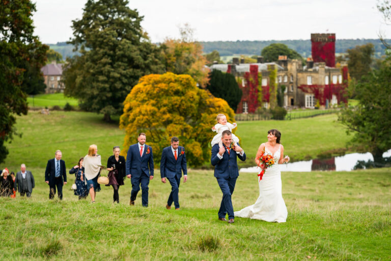 Wedding party walking across countryside estate garden.