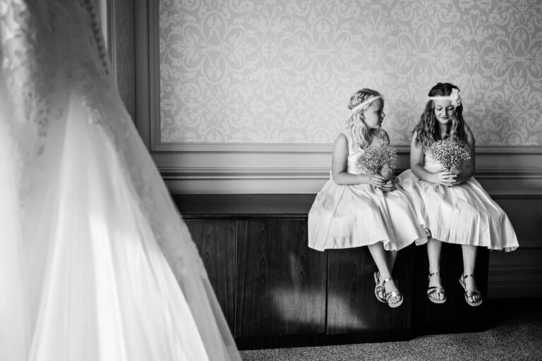 Two flower girls sitting with bouquets, wedding dress visible.