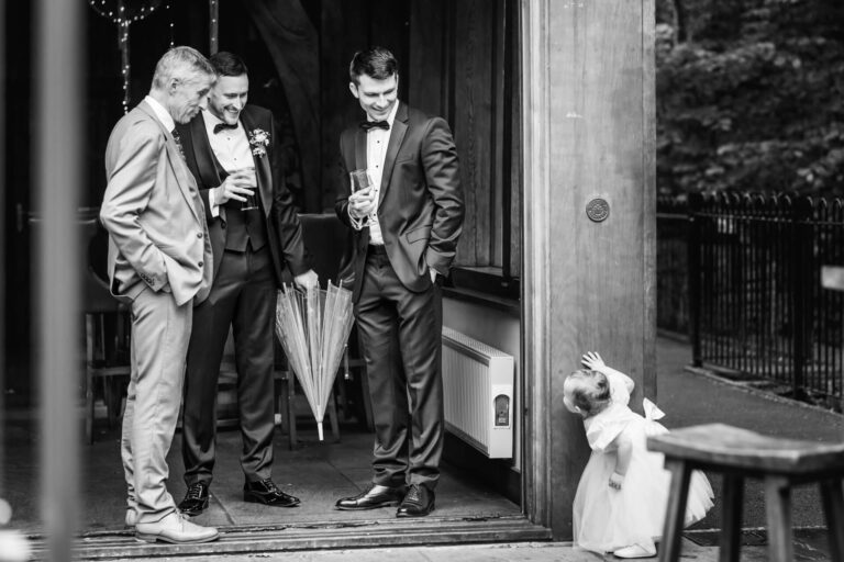 Men in suits laughing, child peeking around doorway.