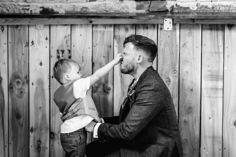 Child playfully pinching man's nose, wooden backdrop.