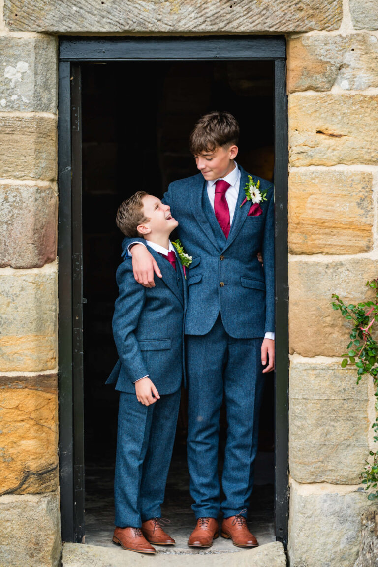 Two boys in suits smiling at each other.