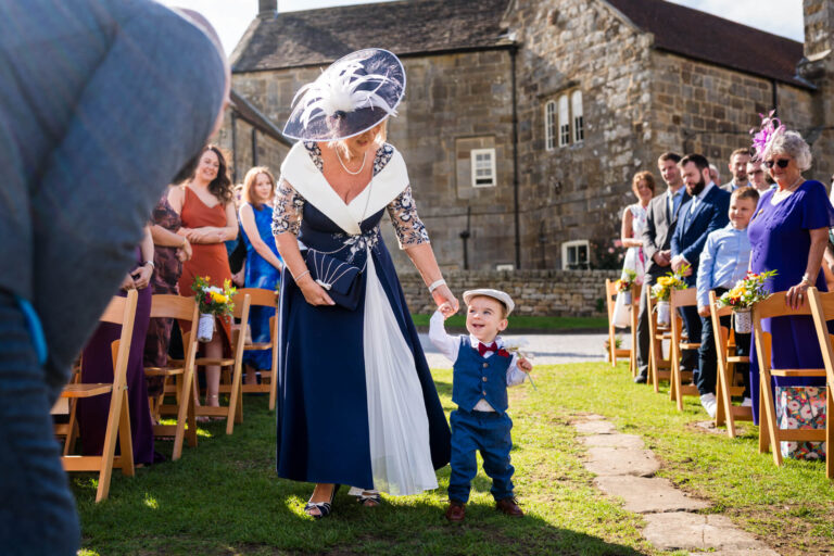 Lady and child walking down wedding aisle outdoors.