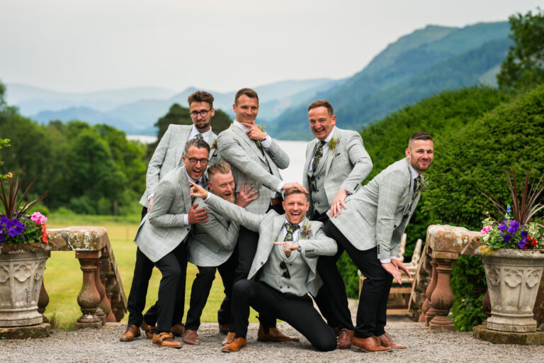 Groomsmen pose playfully in outdoor scenic setting.