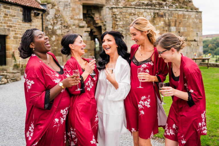 Laughing women in robes with champagne outside.