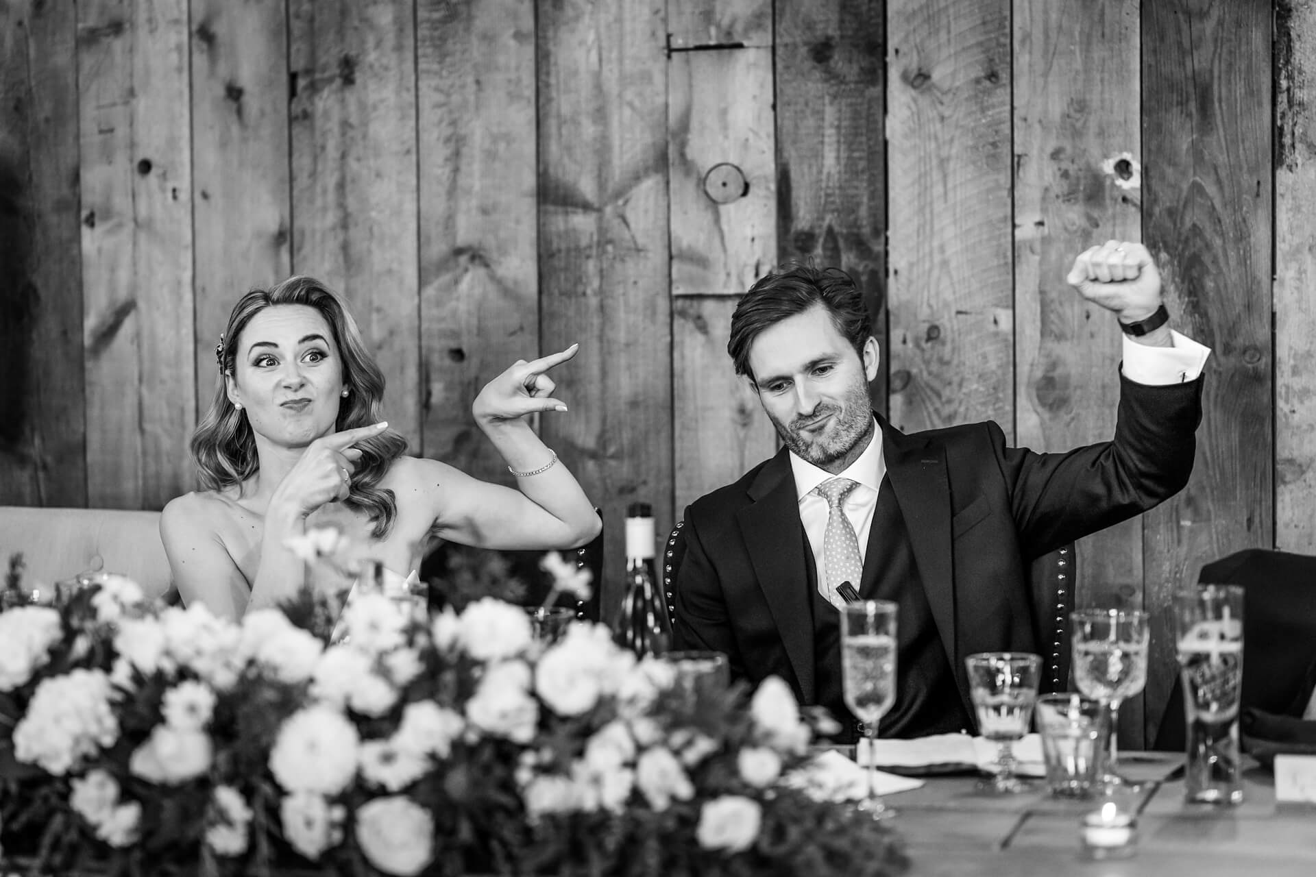 Bride pointing at groom flexing arm at reception